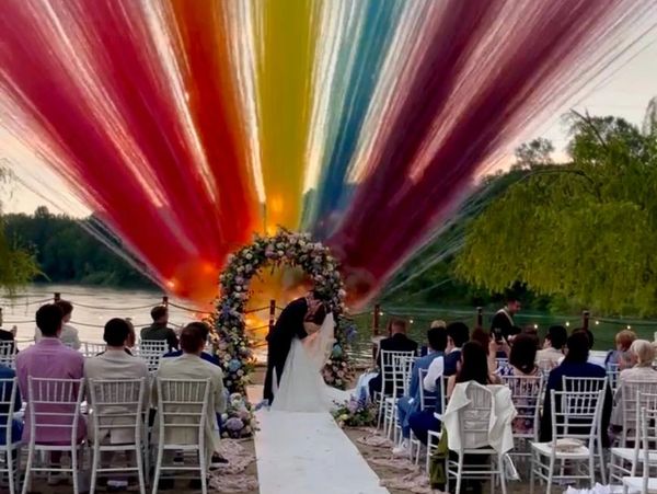 Couple kissing at outdoor wedding with colorful fireworks behind.