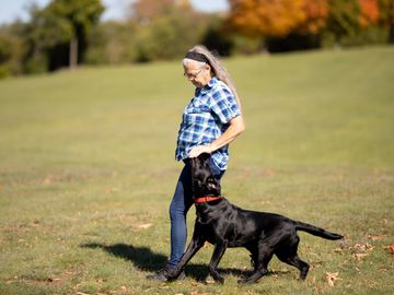 A woman grey hair heels with her dog across a field.