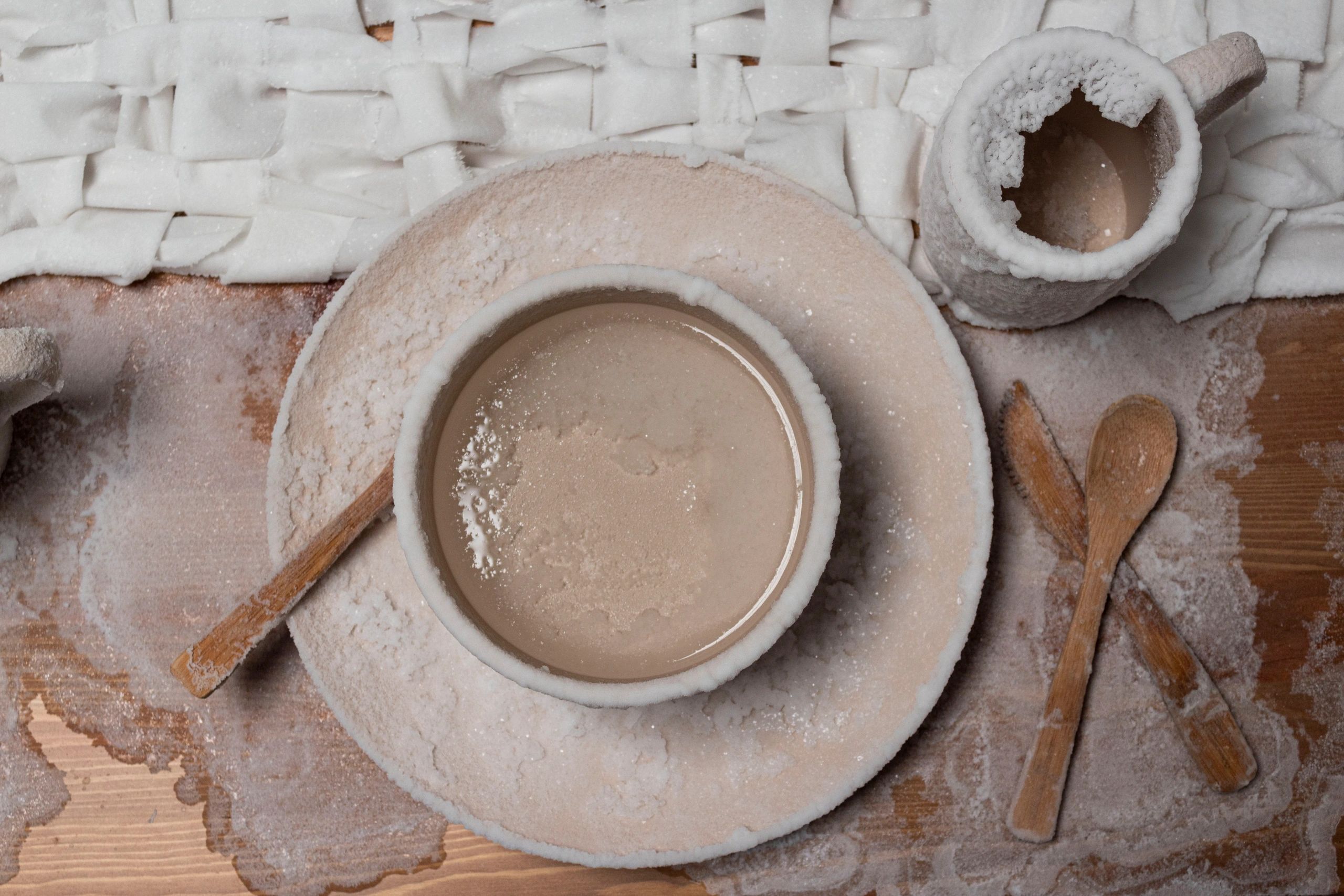 Photograph of a bowl full of salt water sitting on a plate with bamboo silverware with a mug with sa