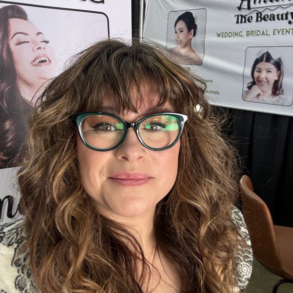 Woman with curly hair and glasses smiling.