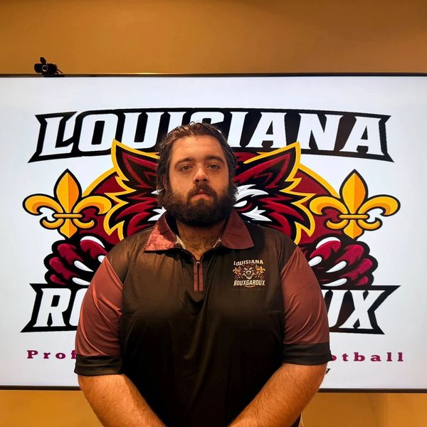 Man in Louisiana Ragin' Cajuns polo shirt standing before team logo.