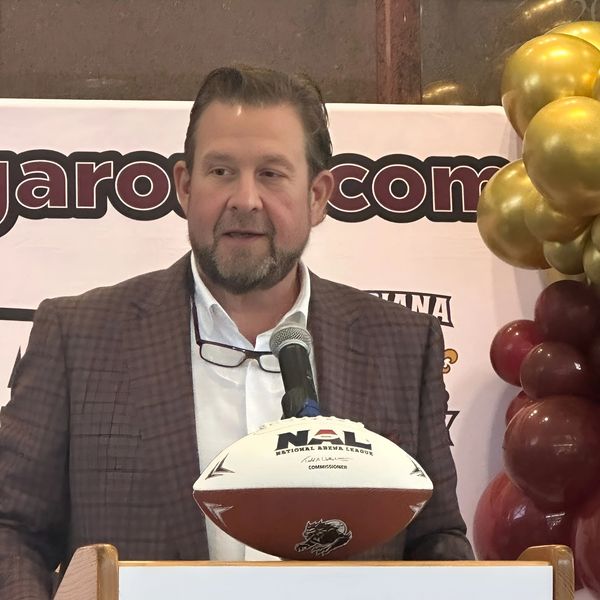 Man speaking at a podium with NAU football and balloons in background.
