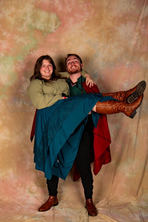 Man joyfully lifts woman in medieval-inspired costumes against a textured backdrop.