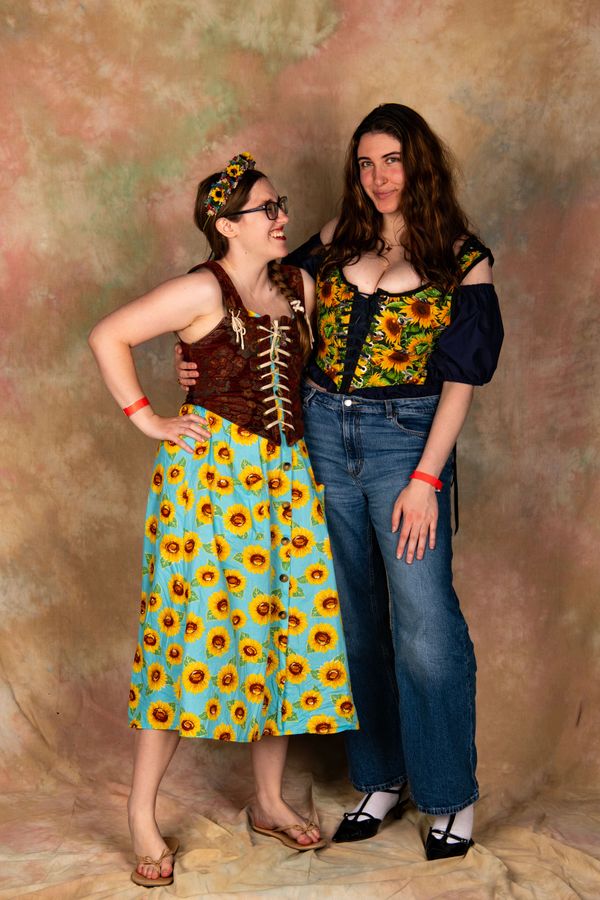 Two women in sunflower-themed outfits posing and smiling against a neutral backdrop.
