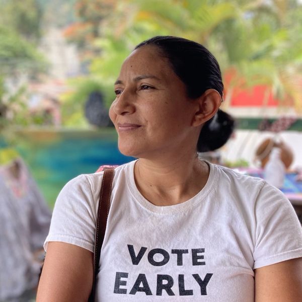 Woman wearing a 'VOTE EARLY' t-shirt smiling outdoors.