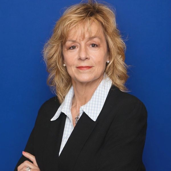 Confident professional woman in a black suit against a blue background.