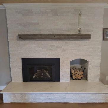 Modern white stone fireplace with wood storage and a wooden mantel.