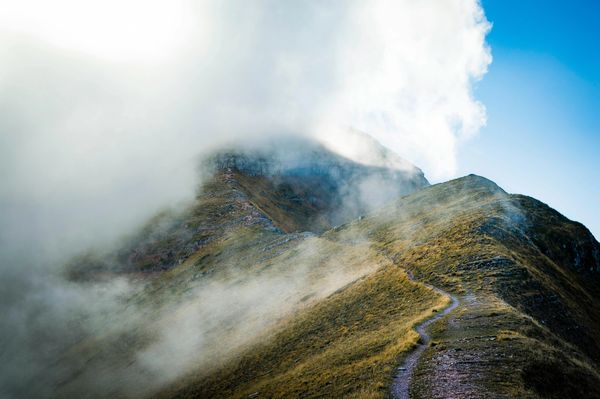 A misty mountain path leading upward under a partly cloudy sky.
