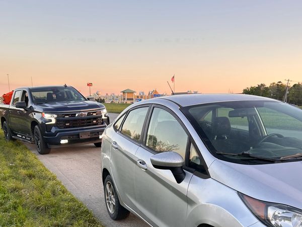 Silver car being towed by a black pickup truck on a road at sunset.