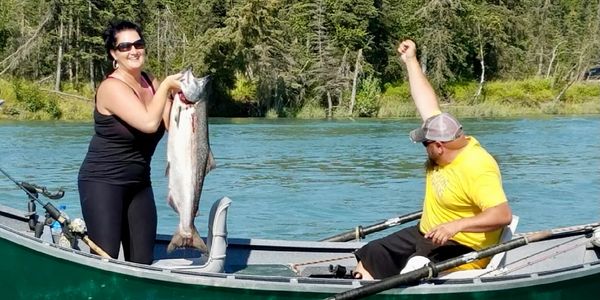 husband and wife on a river boat. husband is celebrating and wife is hold up large silver salmon