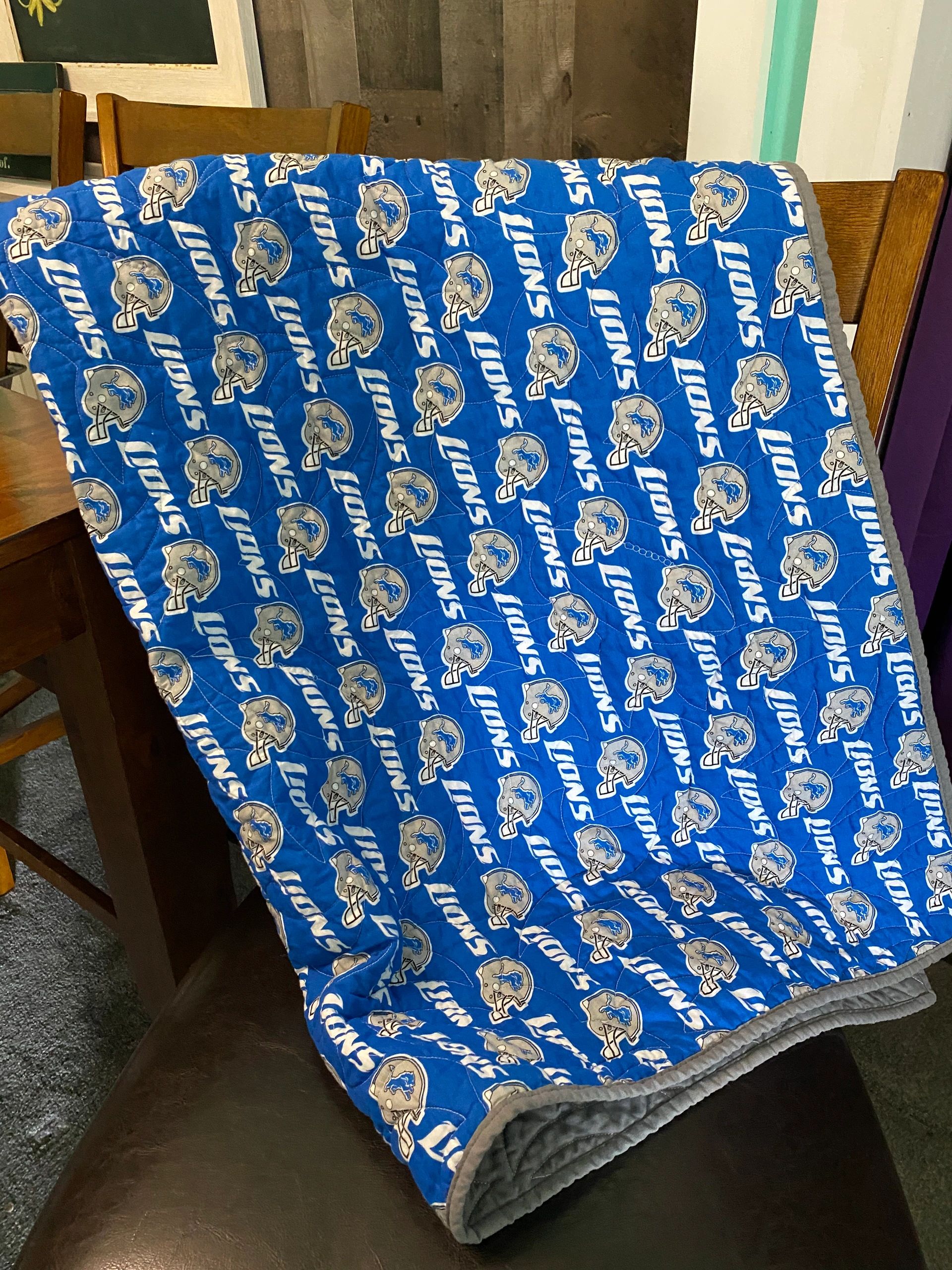 Quilt draped over a chair featuring Detroit Lions logos and helmets.