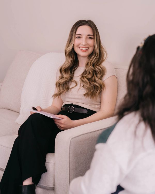 A woman with long wavy hair smiles while holding a notepad during a conversation.