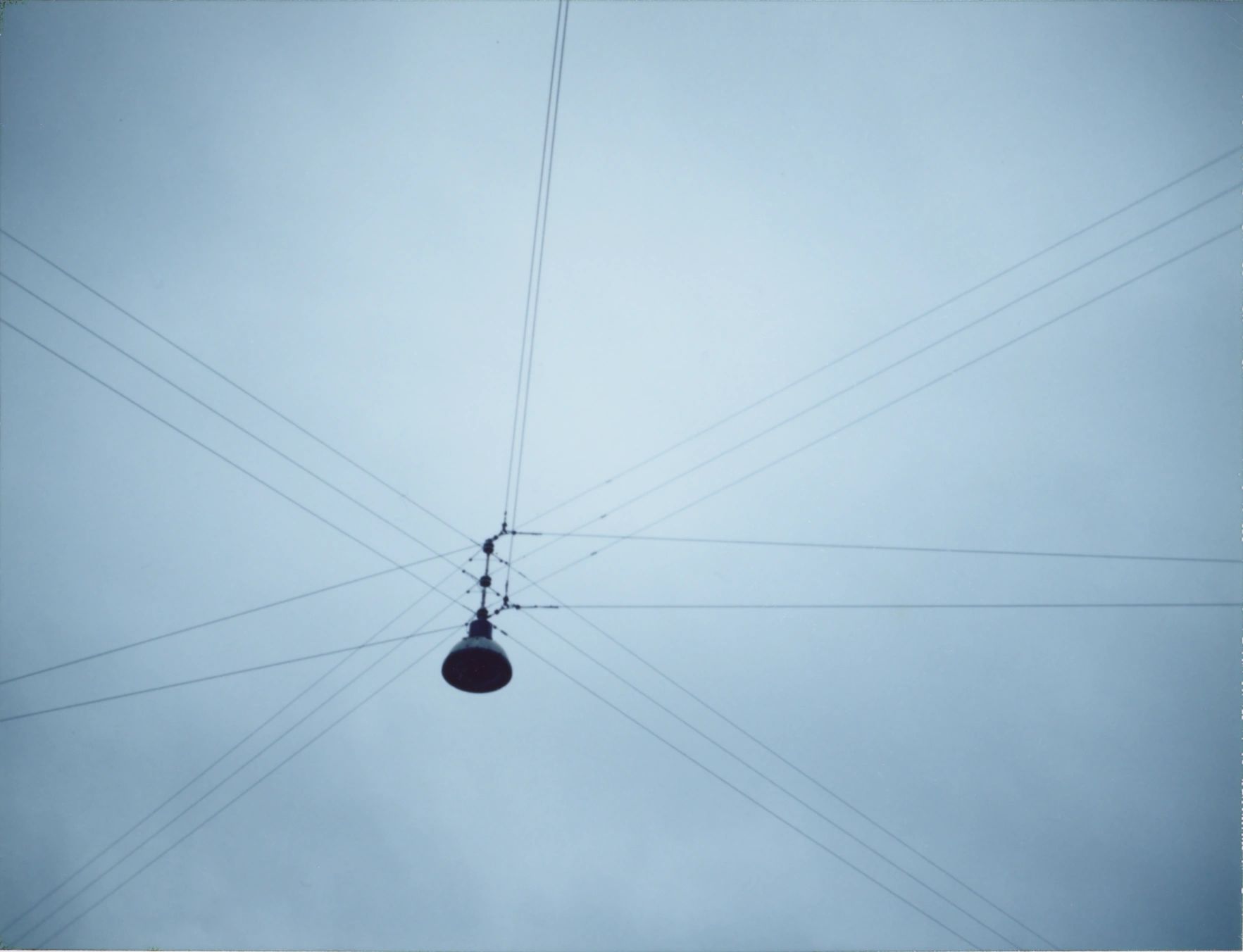 A street lamp suspended by multiple wires against a cloudy sky.