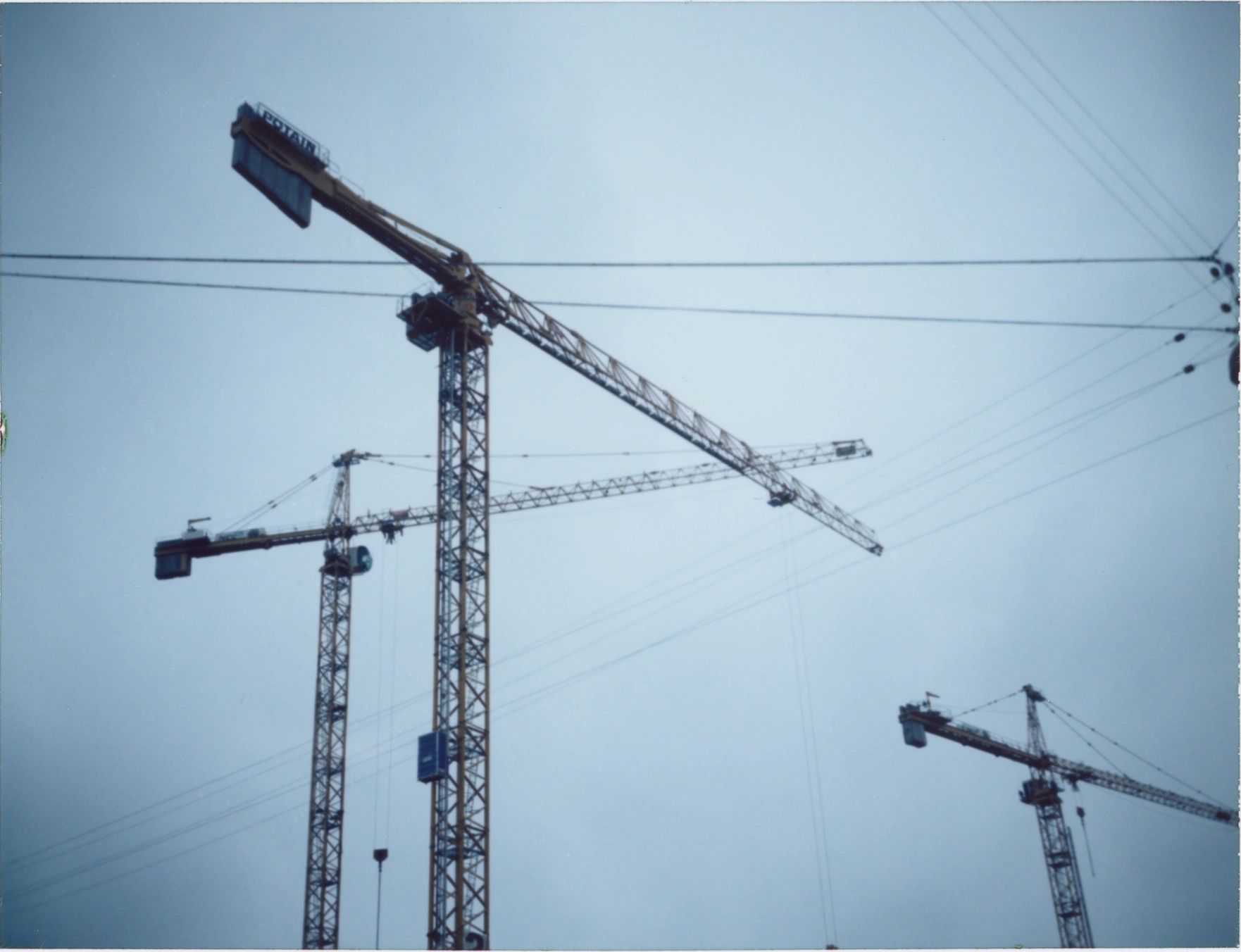 Several construction cranes stand tall against a clear sky.