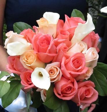 A bouquet of coral and cream roses with white calla lilies and green leaves.