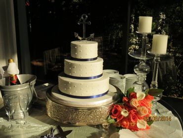 Elegant three-tier white wedding cake with anchor topper and bouquet.