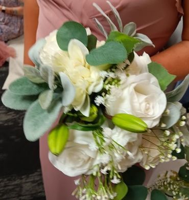 A bouquet with white roses, lilies, and green foliage held by a person in a pink dress.