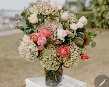 Elegant bouquet of white, pink, and green flowers in a glass vase outdoors.