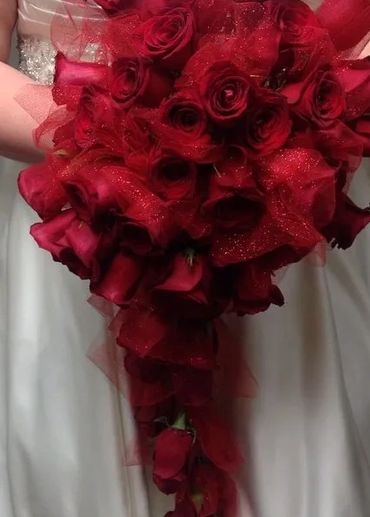 A cascading bouquet of deep red roses held by a person in a white dress.