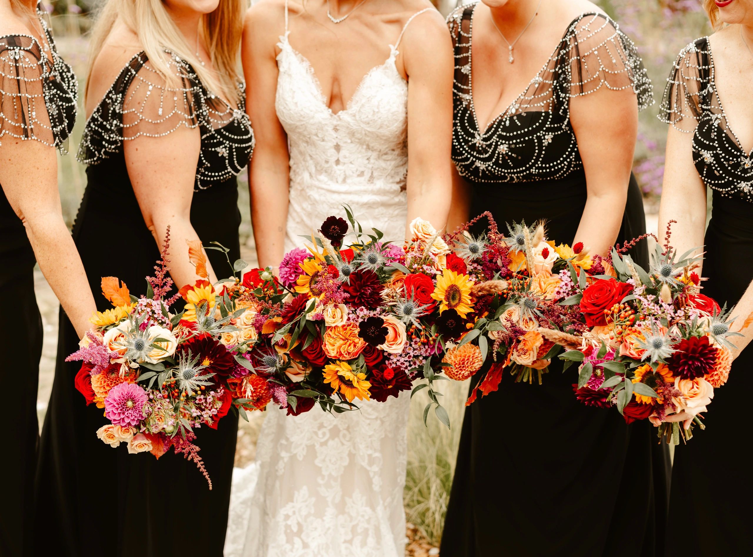 Group of bridesmaids holding bright coloured wedding flowers outdoors.