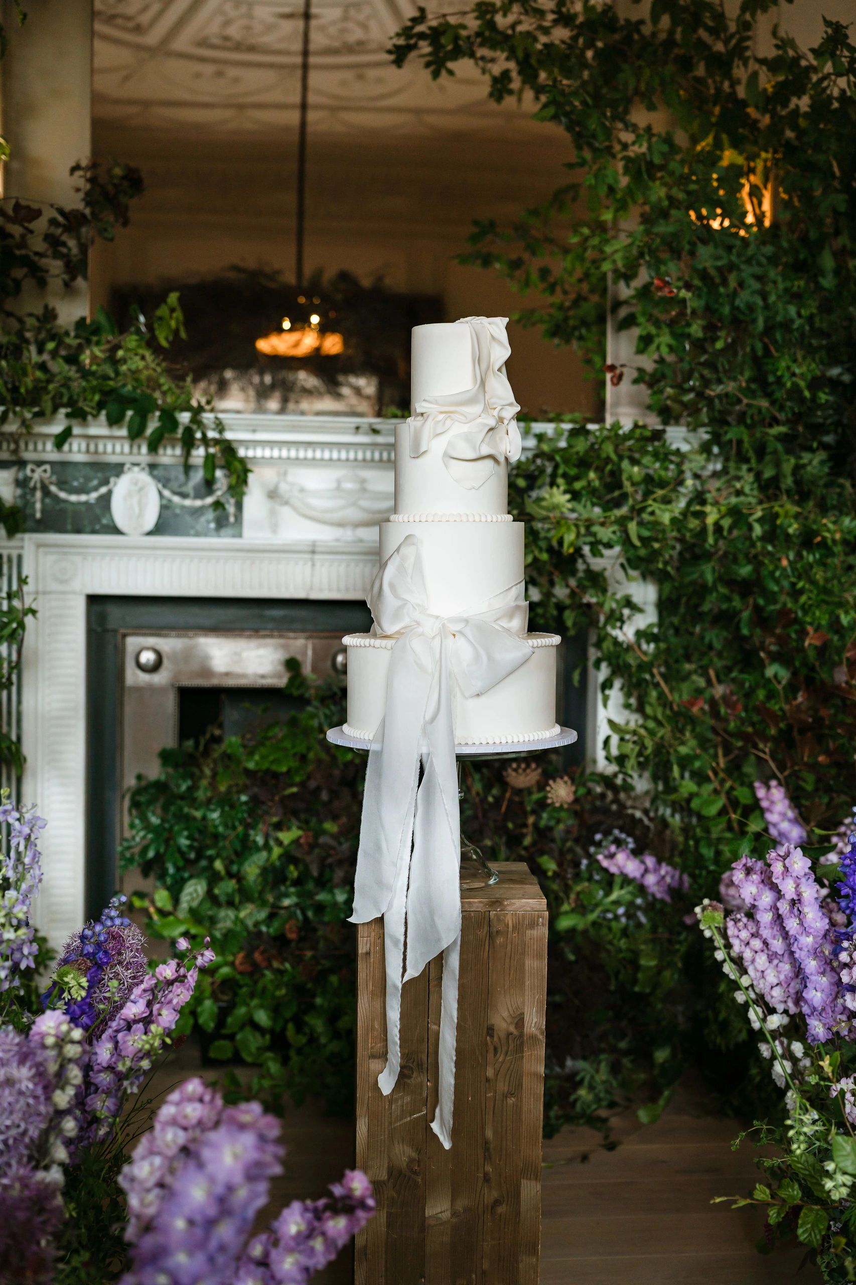 White ribbon wedding cake surrounded by flower meadow and arch. 