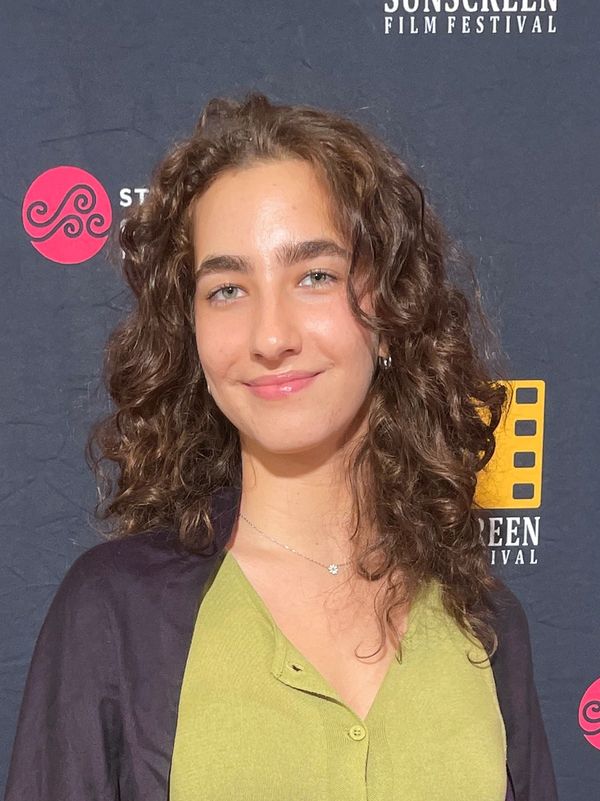 Young woman with curly hair smiling at a film festival backdrop.