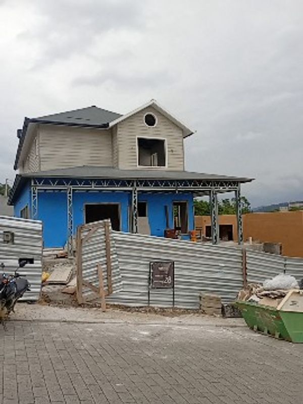 Casa em construção com paredes azuis e cerca metálica.