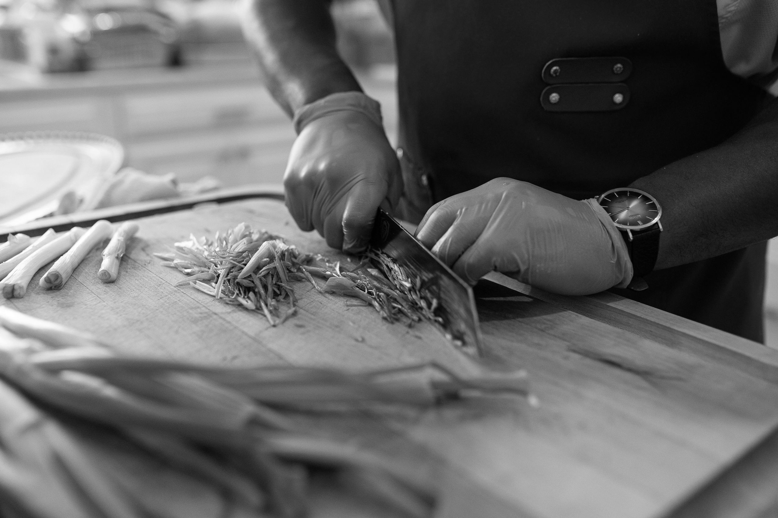 A black and white picture of Chef Dee cutting green onions in a diagonal direction.