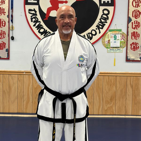 Man in martial arts uniform with black belt standing in dojo.