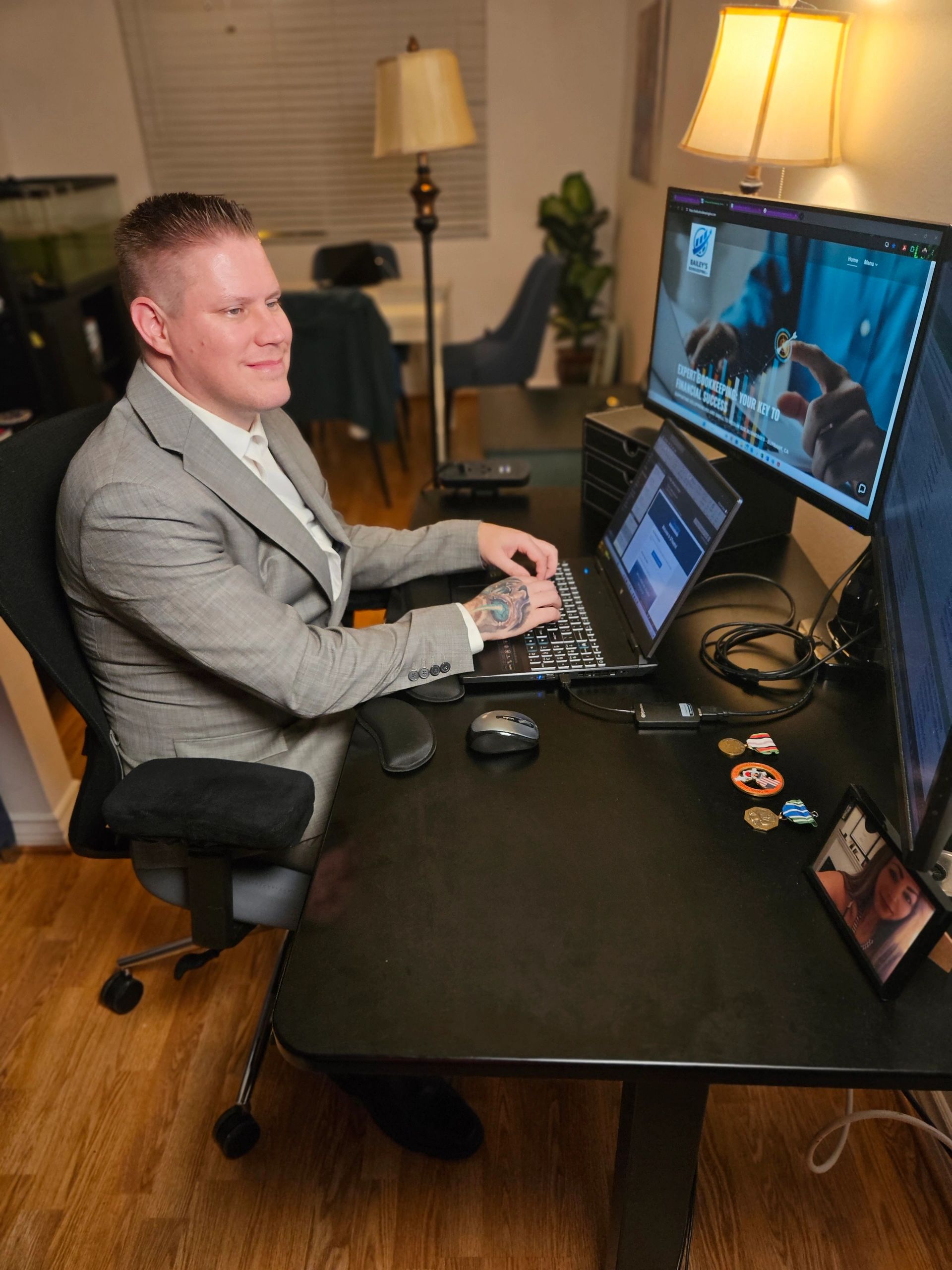 Bailey, Founder/Bookkeeping Pro, smiles while typing on laptop at desk with dual monitors.