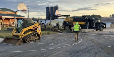Workers operate machinery to resurface a basketball court outdoors.
