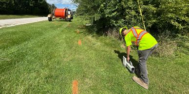 Worker in safety gear marking a line on grass beside a road.