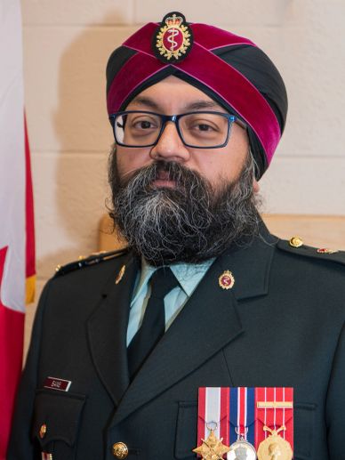 A military officer wearing a decorated uniform and maroon turban with glasses.