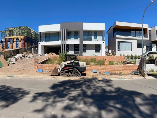 Modern house under construction with machinery in front.