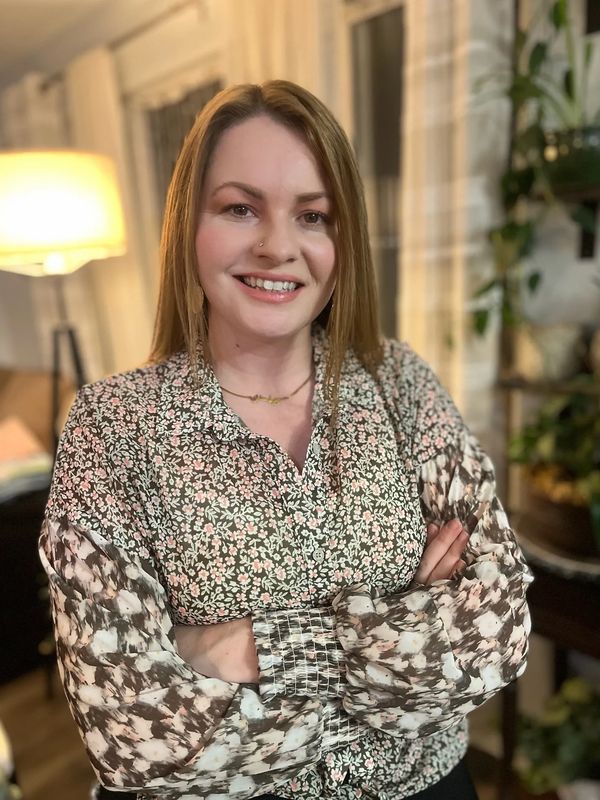 Woman smiling with arms crossed, wearing a floral blouse indoors.