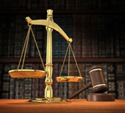 Golden balance scale and wooden gavel on a desk with law books in the background.