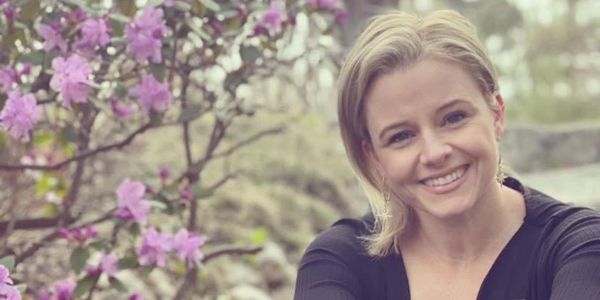 Smiling woman near pink flowers.