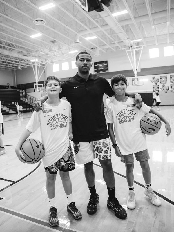 Two boys and a coach pose with basketballs on a gym court.