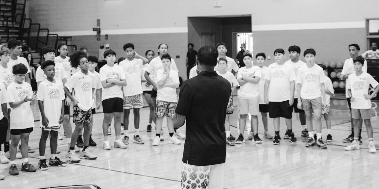 Coach addressing a group of young basketball players in a gym.