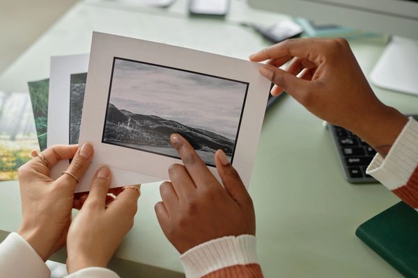 A high-angle close-up shot of two people's hands holding up a matted photograph.