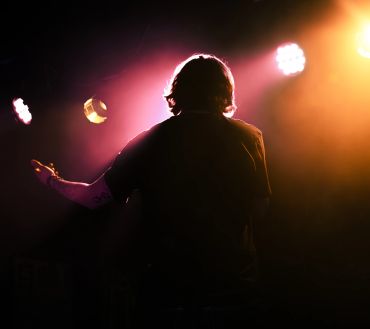 Silhouette of a person juggling against colorful stage lights.