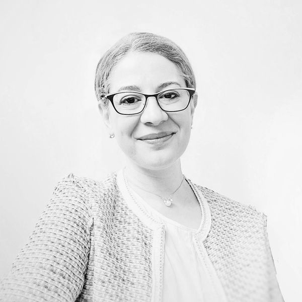 Smiling woman wearing glasses and a textured jacket in a black and white photo.