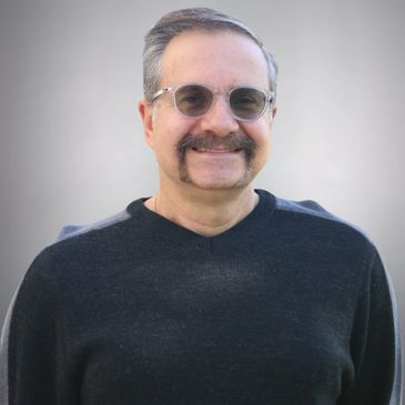 Man smiling with mustache and glasses.