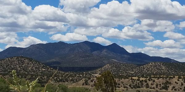 Mountain range under a partly cloudy sky with scattered vegetation.