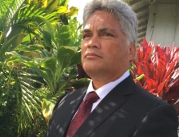 Man in suit standing outdoors with plants in the background.