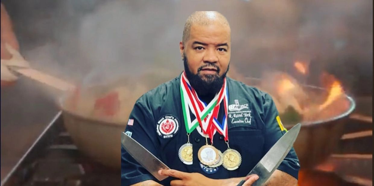 Chef with medals and knives in front of a flaming wok.