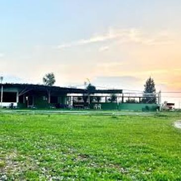 A wide green field with a building and sunset in the background.