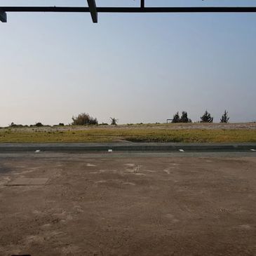 Empty paved area with grass and trees under clear sky.