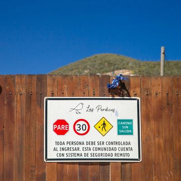 A wooden fence with a Spanish warning sign about community security and speed limits.