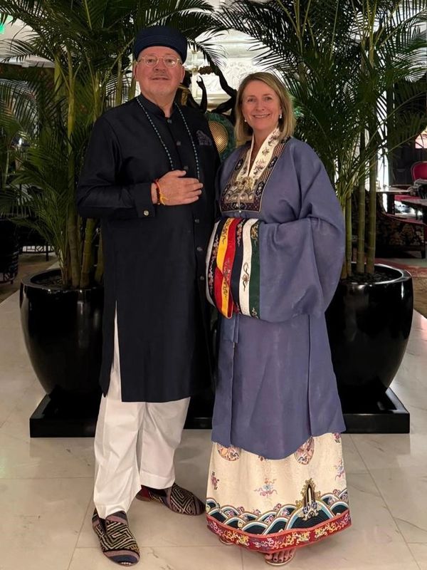 A couple dressed in traditional attire posing indoors with plants in the background.